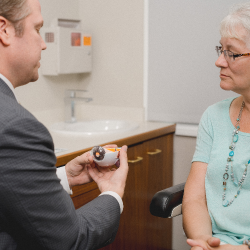 ophthalmologist holding model of an eye to describe cataract surgery to patient during eye exam
