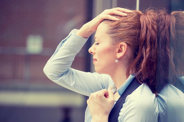 woman leaning against wall hand on head eyes closed